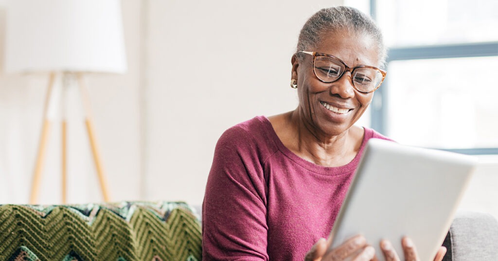 An elderly woman with glasses smiling while looking at a tablet