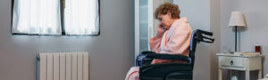 Elderly woman in a wheelchair, with a blanket over her lap, resting her face in her hand