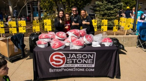 Jason Stone and his team in front of a table piled with helmets, at the Brain Injury Prevention campaign event