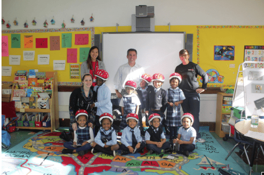 Teachers and students posing together in a classroom, all wearing helmets