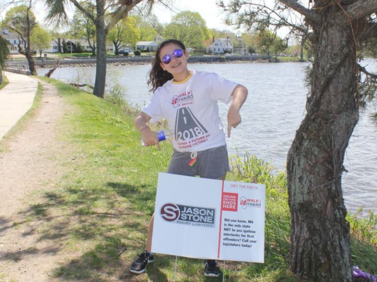 Child pointing to a sign featuring the Jason Stone Injury Lawyers logo, with a message on the side reading 'GET THE FACTS: DRUNK DRIVING ENDS HERE' along with the 'Walk Like MADD' logo