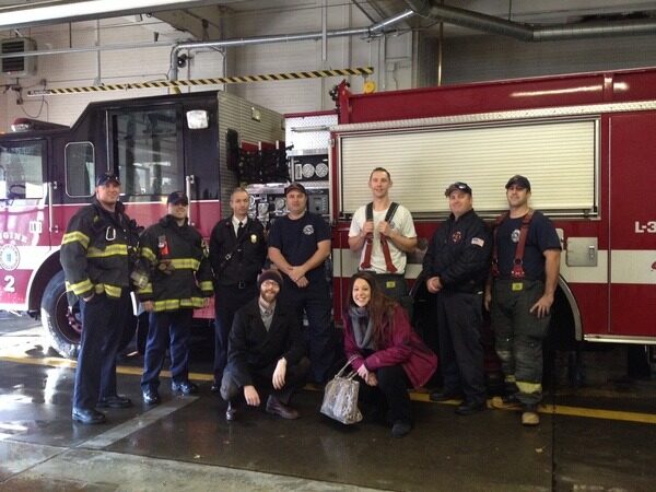 Jason Stone's team posing in front of a fire truck with firefighters.