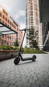 A modern electric scooter parked on a paved walkway between high-rise buildings, indicating urban micromobility and a focus on eco-friendly transportation in a city environment